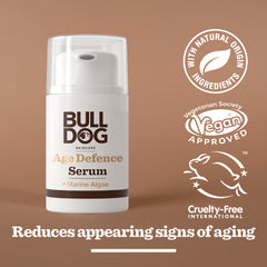 A bottle of Age Defence Serum with labels for natural origin ingredients, vegan approval, cruelty-free certification, and the claim: reduces fine lines and wrinkles, set against a brown background.